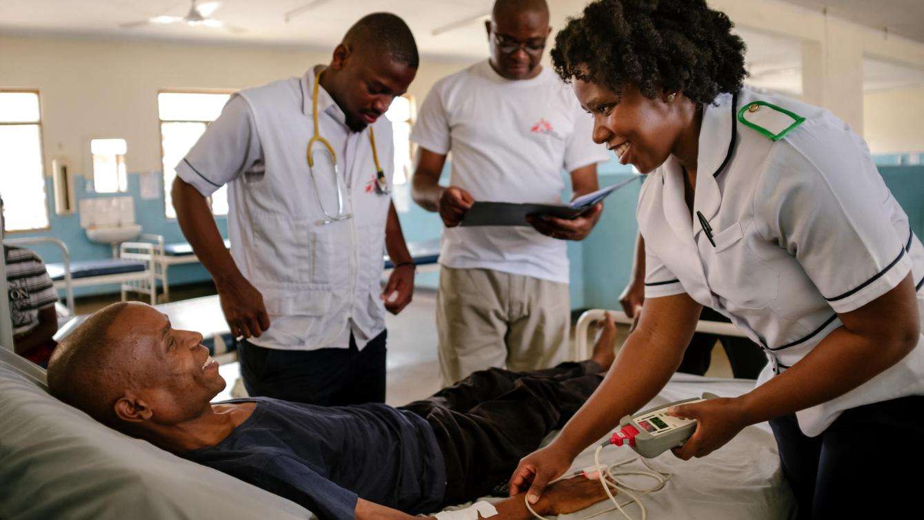 A group of MSF medics gathered around a patient in a hospital bed.