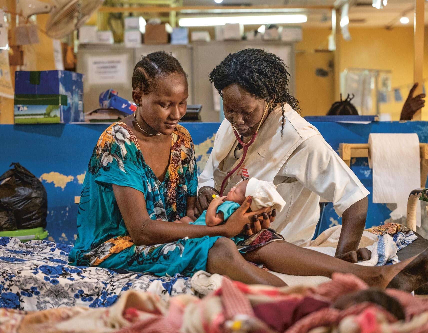 An MSF nurse and patient sit on a hospital bed with a newborn baby in Aweil, South Sudan.