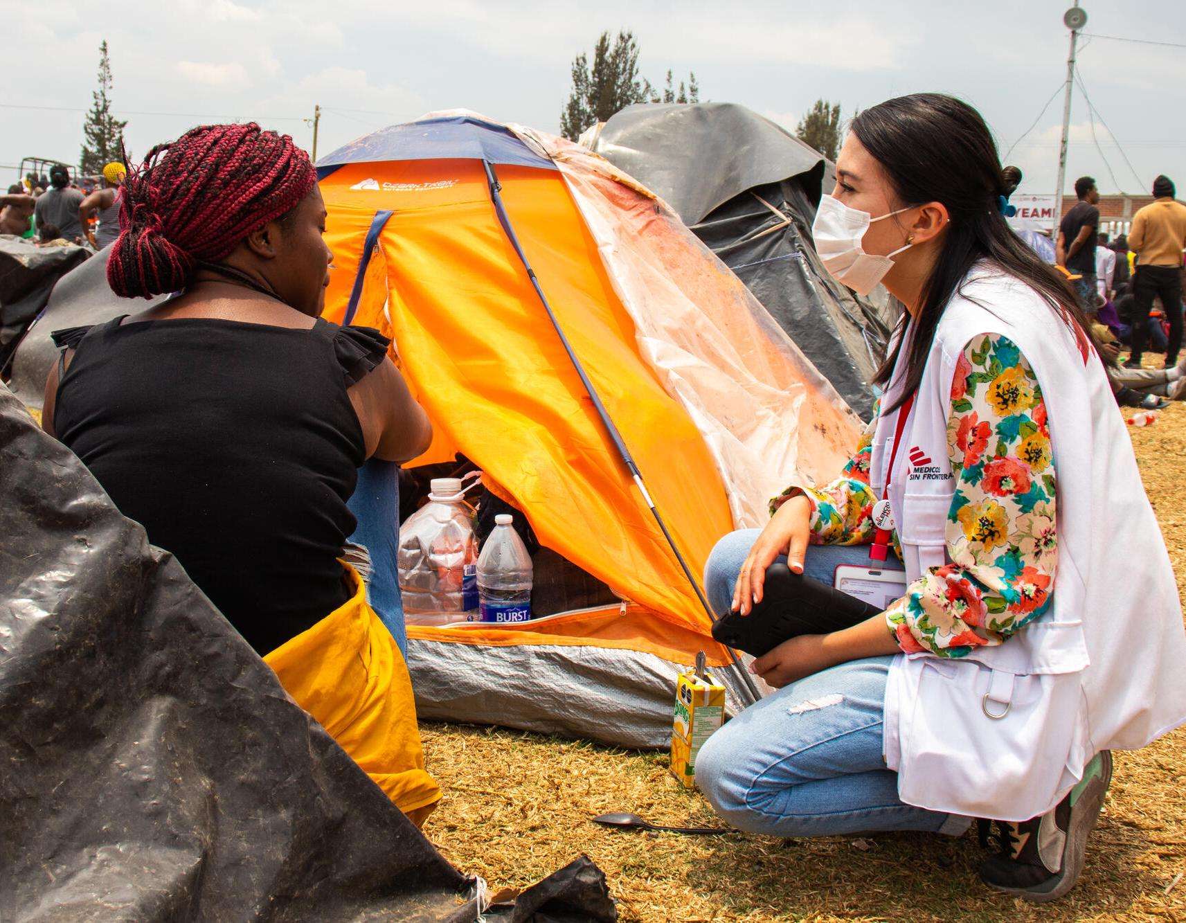 A migrant woman sitting next to her tent speaks to a MSF worker. 