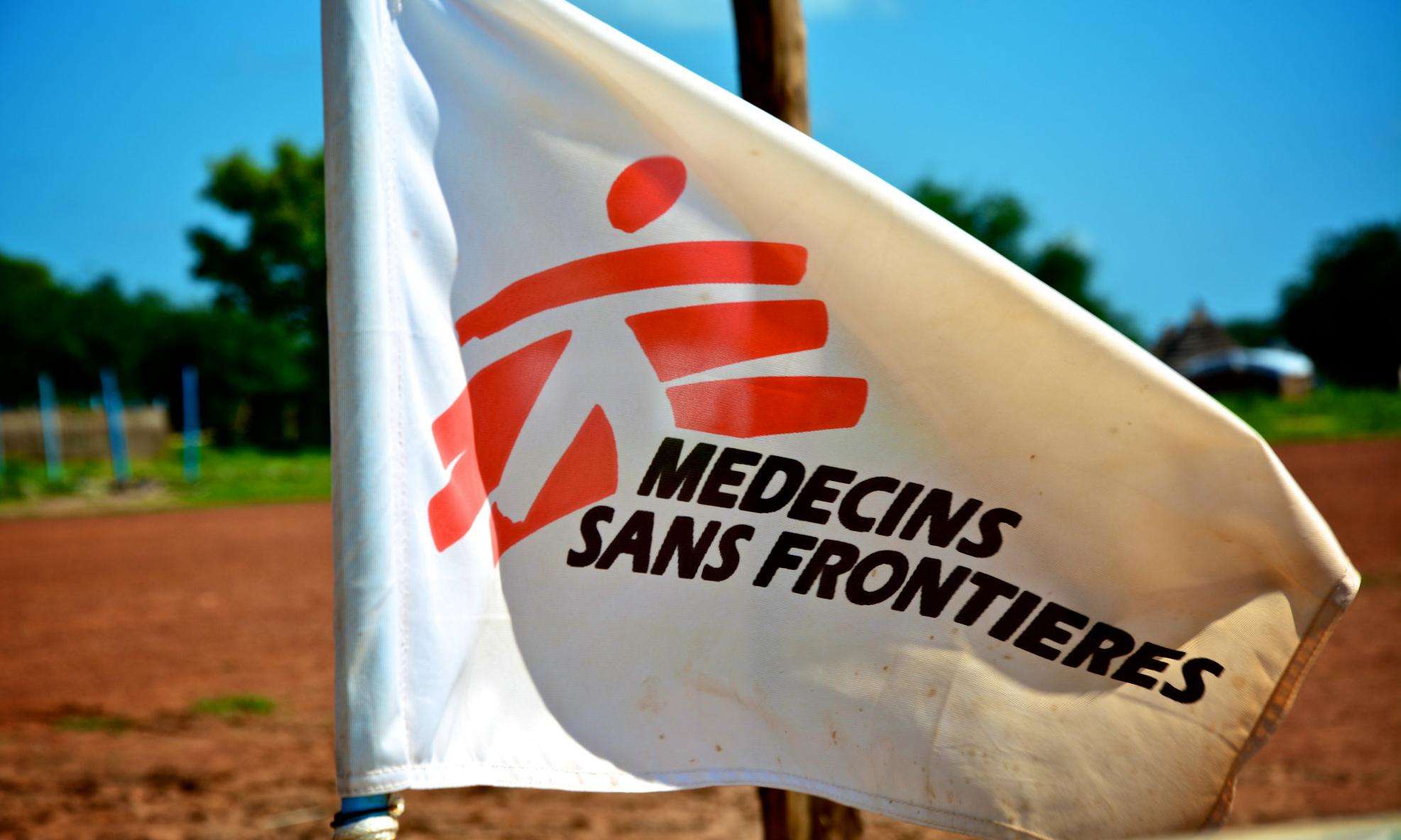 White flag with red logo of Doctors Without Borders/Médecins Sans Frontières (MSF) against sunny blue sky