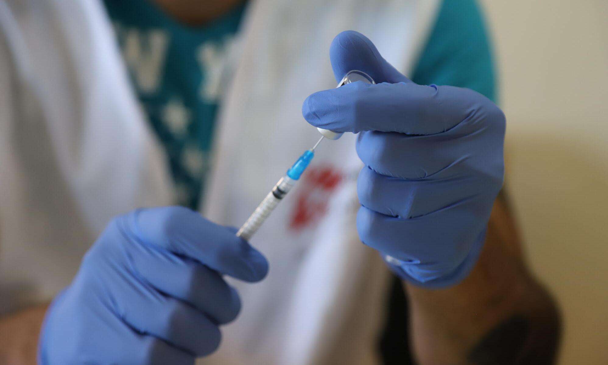 An MSF staff member in white vest and latex gloves prepares a dose of the COVID-19 vaccine at a nursing home in Lebanon.