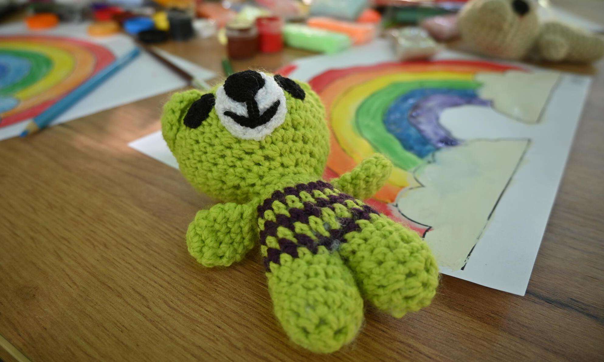 green knit toy lays on wooden table with drawing of a rainbow