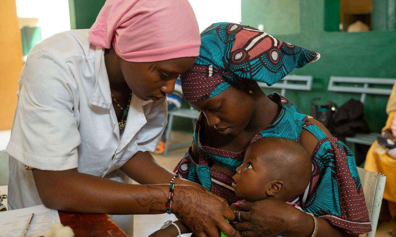 A mother holder her child while he is examined by a nurse in Niono, Mali 