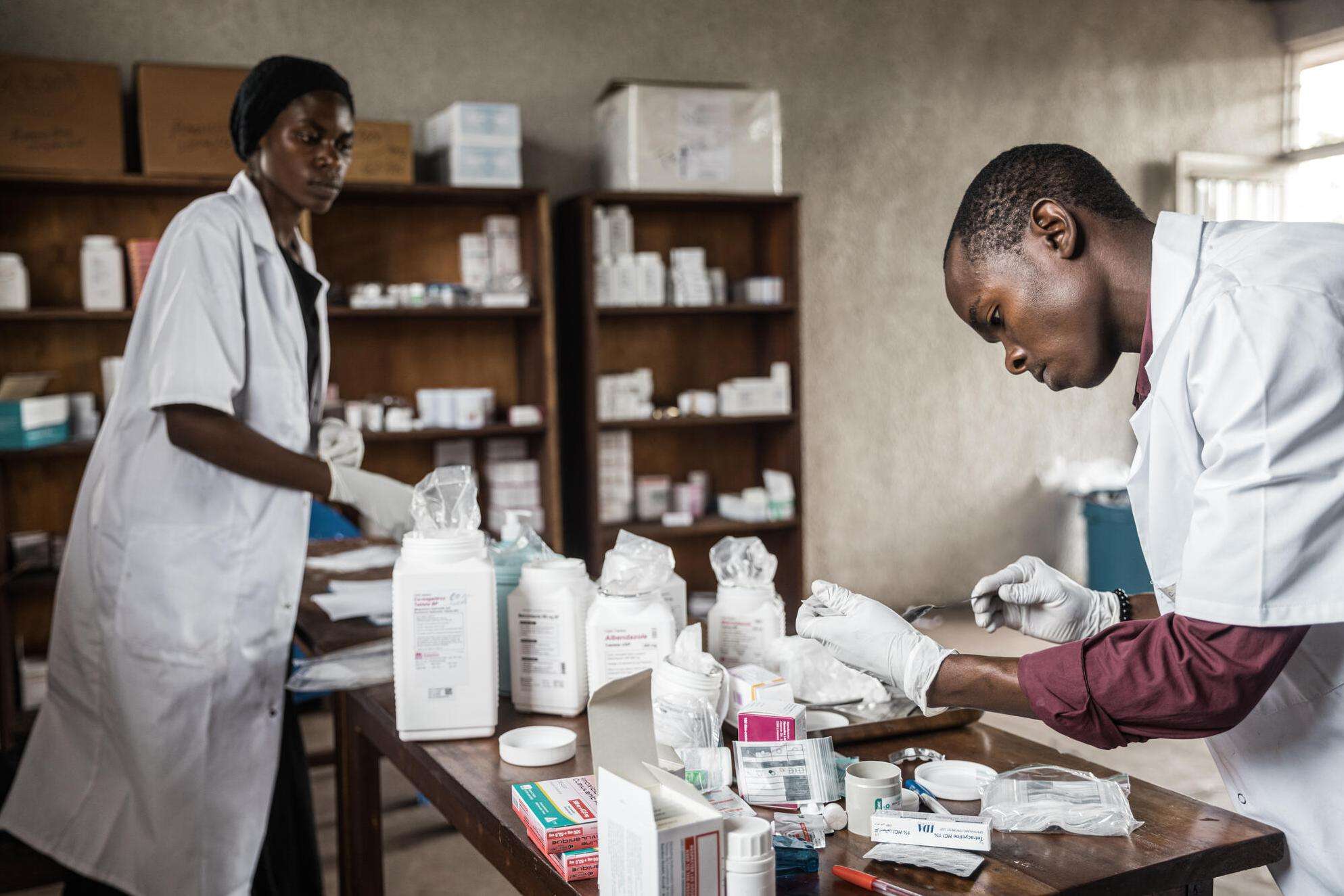 Two medics in white suits are in an office looking through medications together on a table.