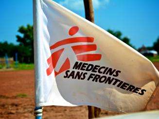 White flag with red logo of Doctors Without Borders/Médecins Sans Frontières (MSF) against sunny blue sky