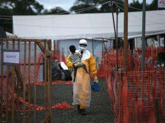 An MSF health worker carries a child suspected of having Ebola.