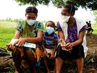 A child sits between two people in surgical masks after completing TB treatment from MSF in Papua New Guinea.