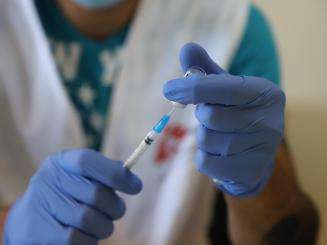 An MSF staff member in white vest and latex gloves prepares a dose of the COVID-19 vaccine at a nursing home in Lebanon.