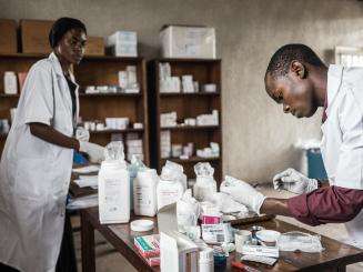 Two medics in white suits are in an office looking through medications together on a table.