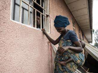 A woman, outside of a building, speaking to a pharmacist through a window. They are both smiling at each other.