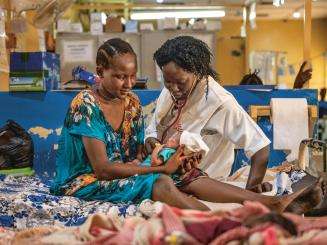 An MSF nurse and patient sit on a hospital bed with a newborn baby in Aweil, South Sudan.