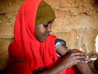 A young girl in a red headscarf injects insulin in Kenya.