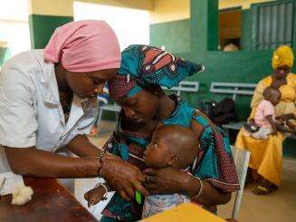 A mother holder her child while he is examined by a nurse in Niono, Mali 