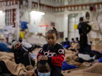 A child stands next to a caregiver on the deck of a search and rescue ship. 