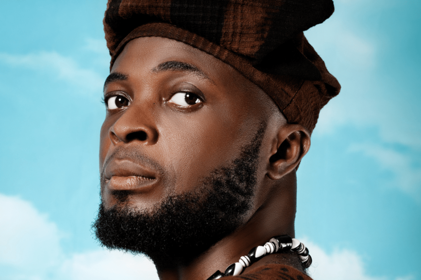 Man with beard, necklace, and hat against blue sky background.