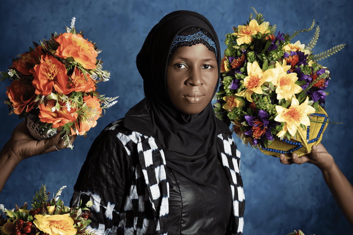 A woman in checker print dress surrounded by bouquets of flowers. 