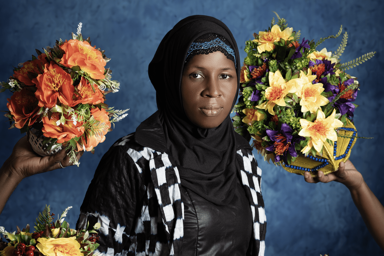 A woman in checker print dress surrounded by bouquets of flowers. 