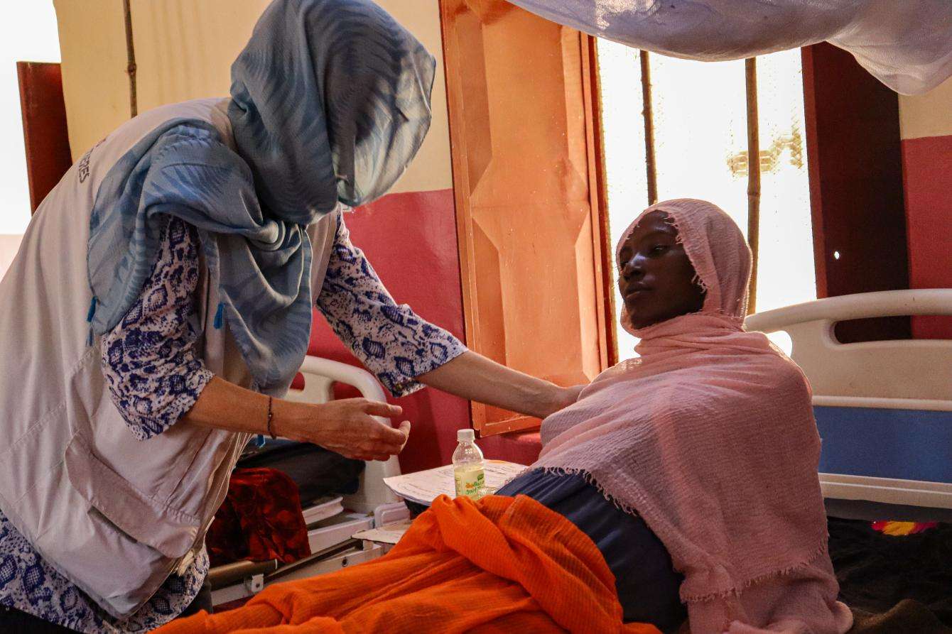 A staff member helps a woman on a hospital bed in South Darfur, Sudan.