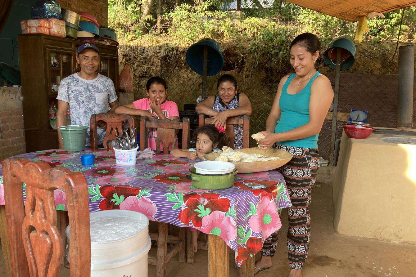 A family sits around at table outside, smiling.