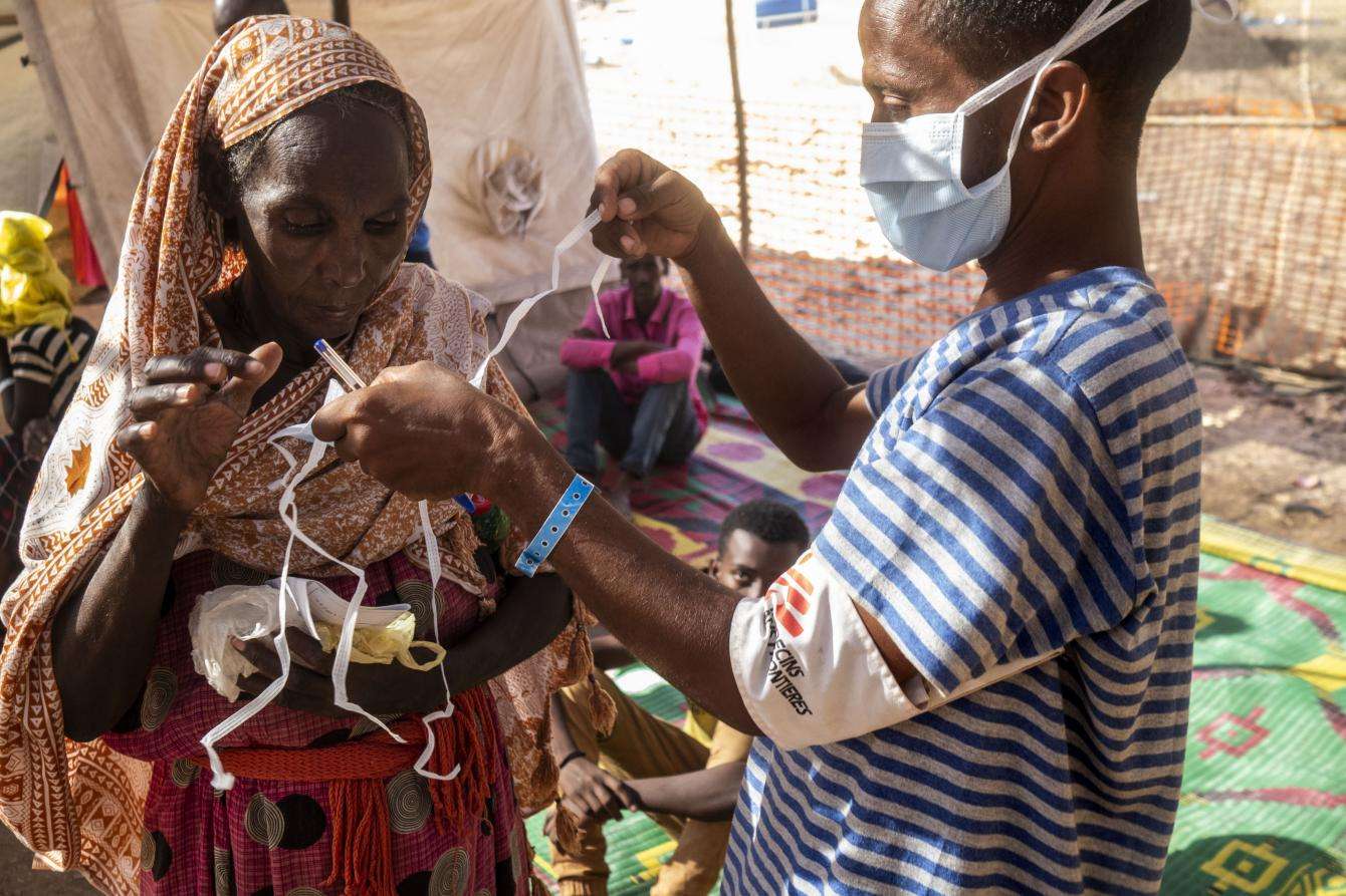 A medic helps a woman put on a mask.