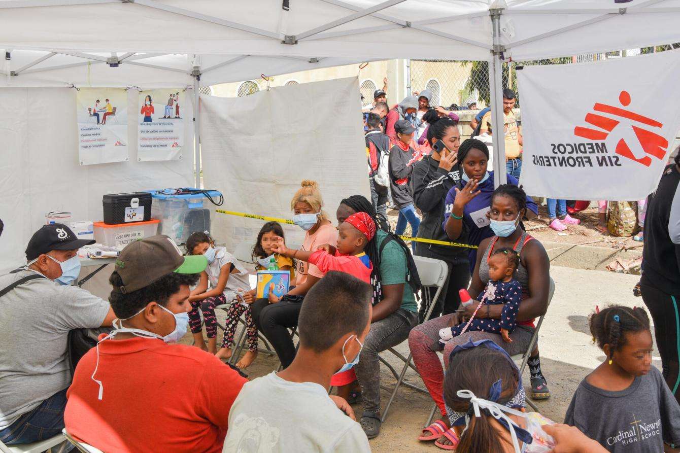 A group of people are gathered under a crowded white MSF tent.