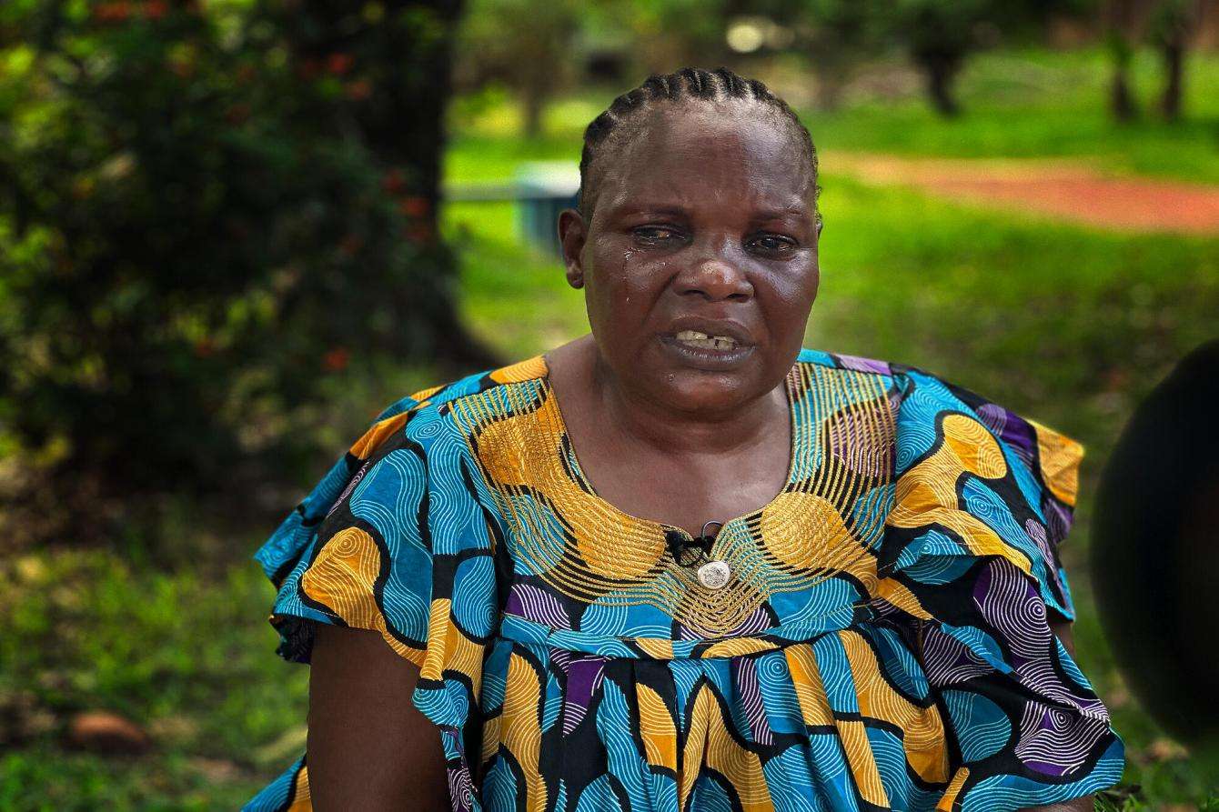 A woman in a bright orange and blue dress sits in a green area in the Central African Republic.