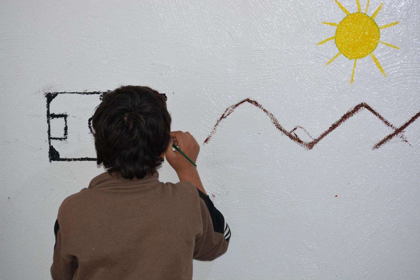 A child draws a sun and mountains on the wall during an art therapy session in Al-Hol camp, northeast Syria.