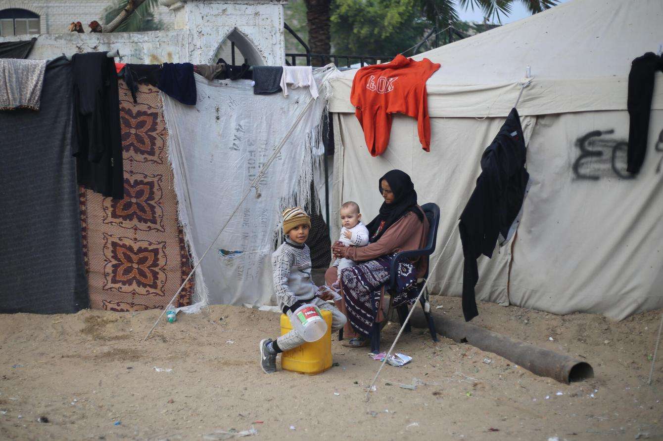 A displaced Palestinian woman with her children outside a makeshift tent in Gaza.