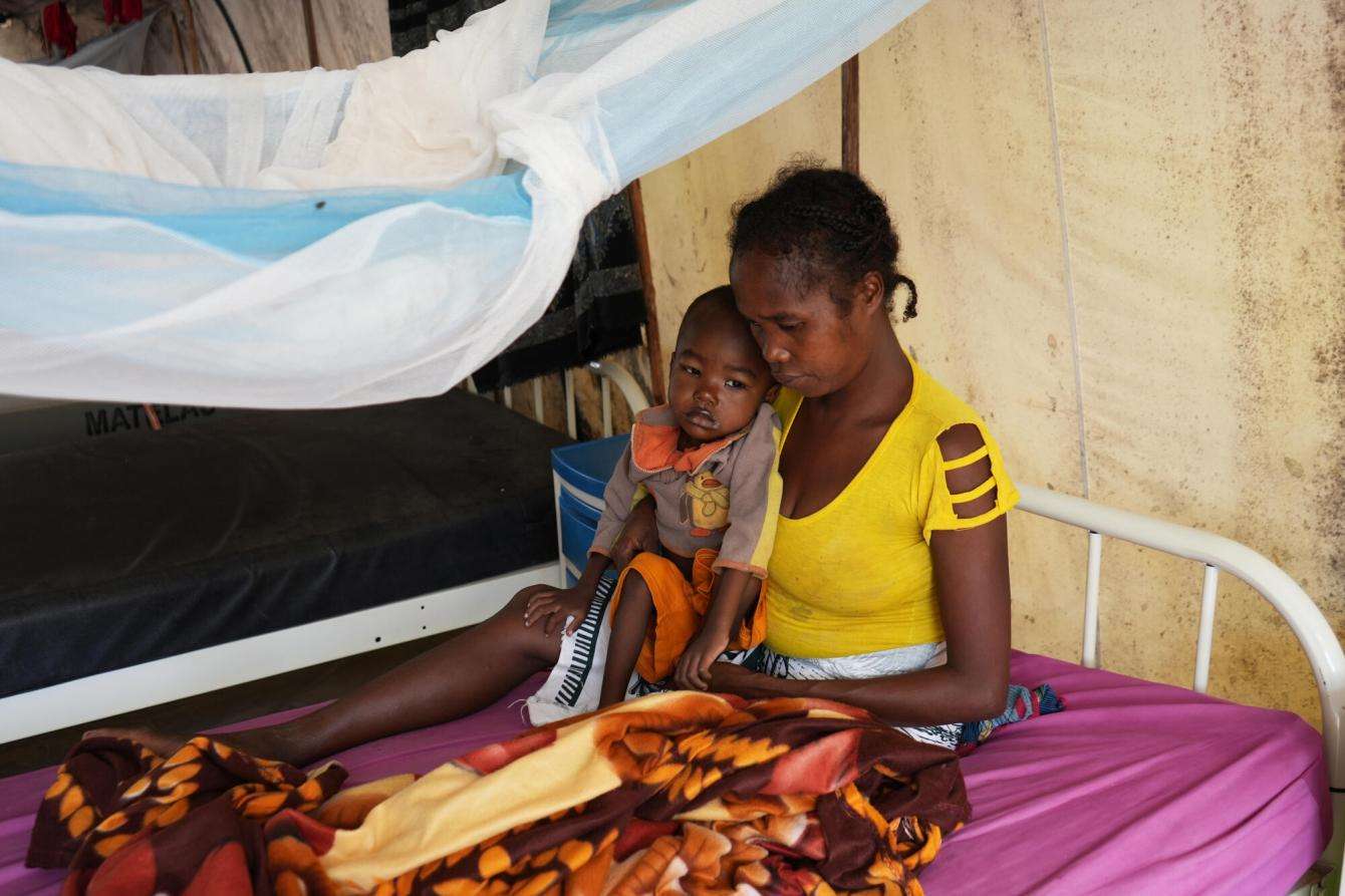 A mother cradles her child in her lap on a hospital bed. 