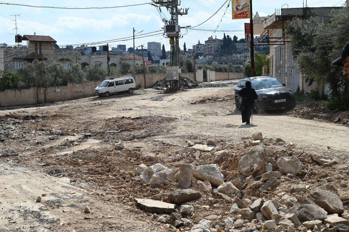 A woman walks on a dirt road amid rubble to cars in the West bank, Palestine. 