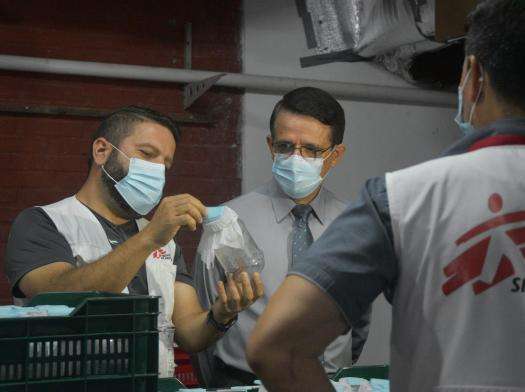 A group of men wearing masks in a lab are looking at a jar of mosquitos together.