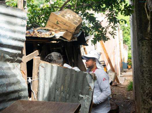 A man in an MSF vest stands next to a tin-ribbed structure speaking to someone inside. 