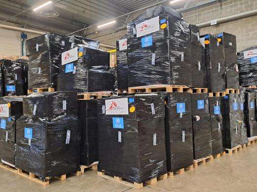 Boxes of medical donations piled on a pallet in a warehouse.