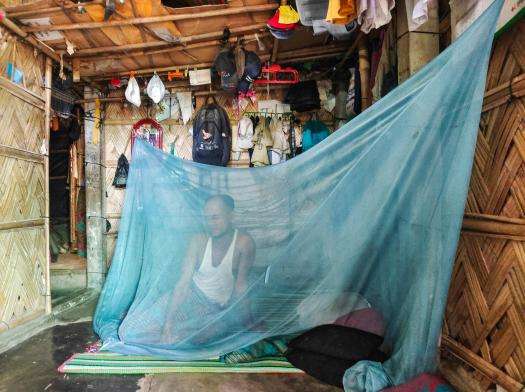 A Rohingya man behind a blue mosquito net in Cox's Bazar, Bangladesh.