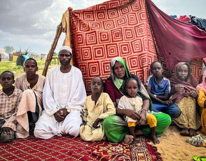 A family of Sudanese refugees sit in front of a makeshift tent in a refugee camp in Chad