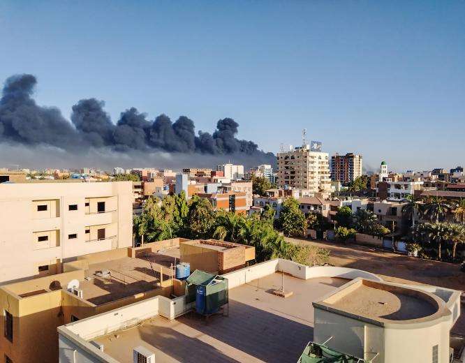 A scene of the city of Khartoum and a billowing fire in the background.