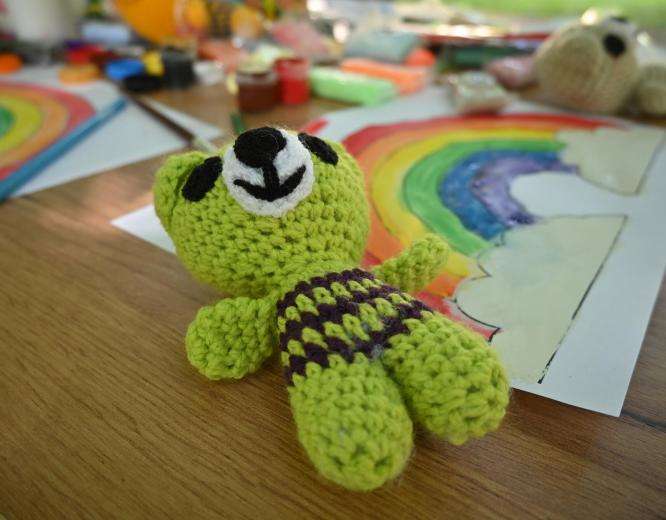 green knit toy lays on wooden table with drawing of a rainbow