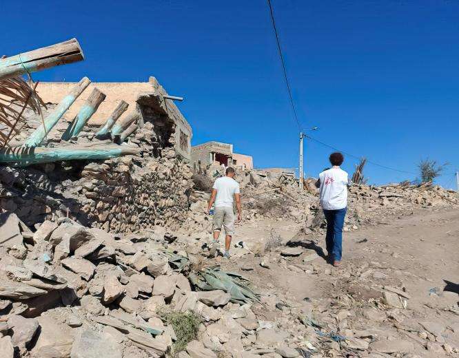 Two people with MSF logos on their shirts walking amidst the concrete wreckage of the earthquake.