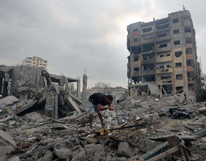 A man drinks water from a pipe on the wreckage from Israeli airstrikes in Gaza in 2023.