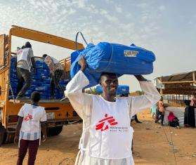 A man carries plastic sheeting to distribute in a displacement camp in Chad. 