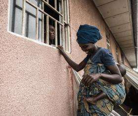 A woman, outside of a building, speaking to a pharmacist through a window. They are both smiling at each other.