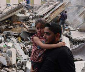 A man holding a child with wreckage from Israeli bombardment in Gaza behind them.