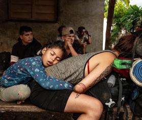 A child sits behind his mother who is crouching down on a bench after crossing the Darién Gap.