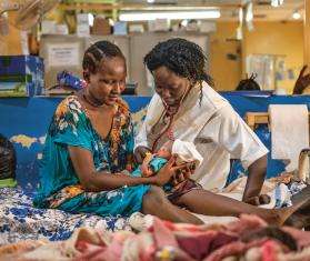 An MSF nurse and patient sit on a hospital bed with a newborn baby in Aweil, South Sudan.