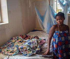 Woman standing next to her newborn twins resting on a hospital bed. 