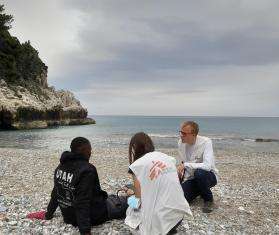 A man sits on the shores of Greece and is tended to by two MSF workers. 