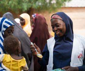 MSF health promoter lets a child taste test Tom Brown, a nutrient-rick porridge, in Nigeria. 