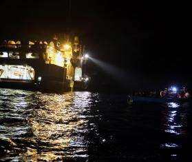 The Geo Barents recue vessel shines a light on a small boat at night in the central Mediterranean.